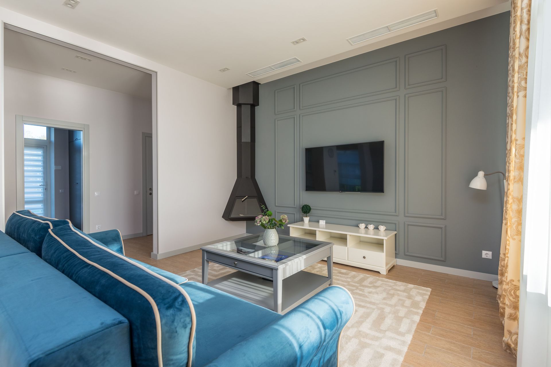 A stylish living room featuring a blue couch, wall-mounted TV, and elegant decor.